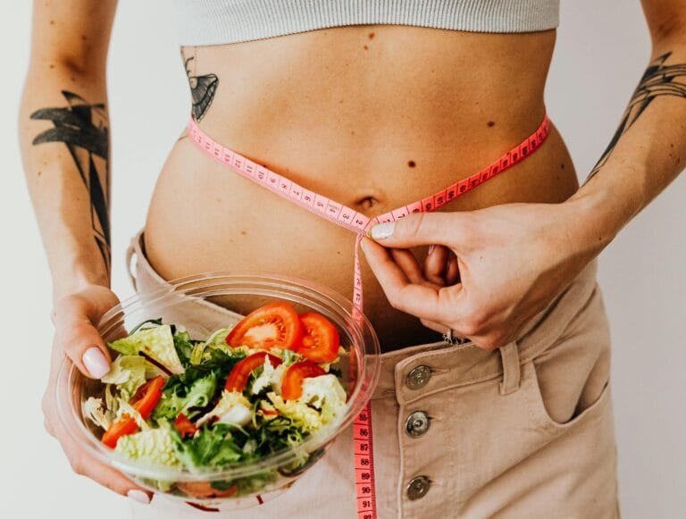 Une jeune femme sportive tient une assiette de légume et mesure la taille de son ventre